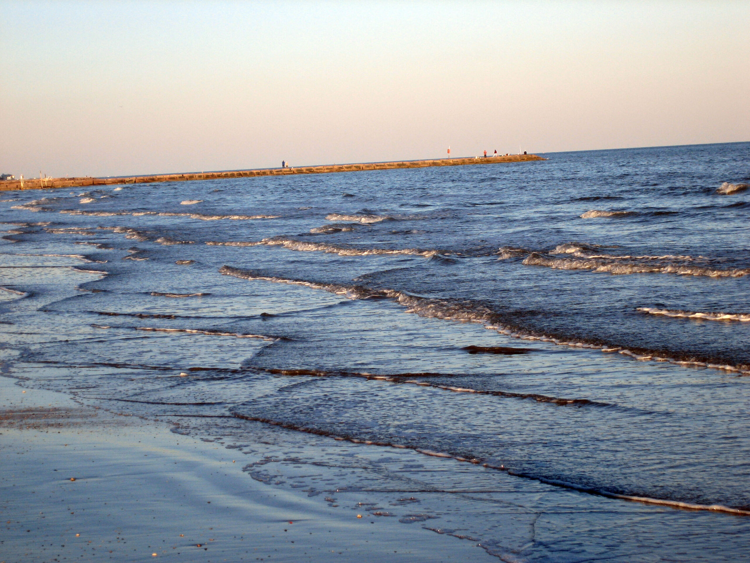 Waves at Galveston beach featuring a jetty in the background