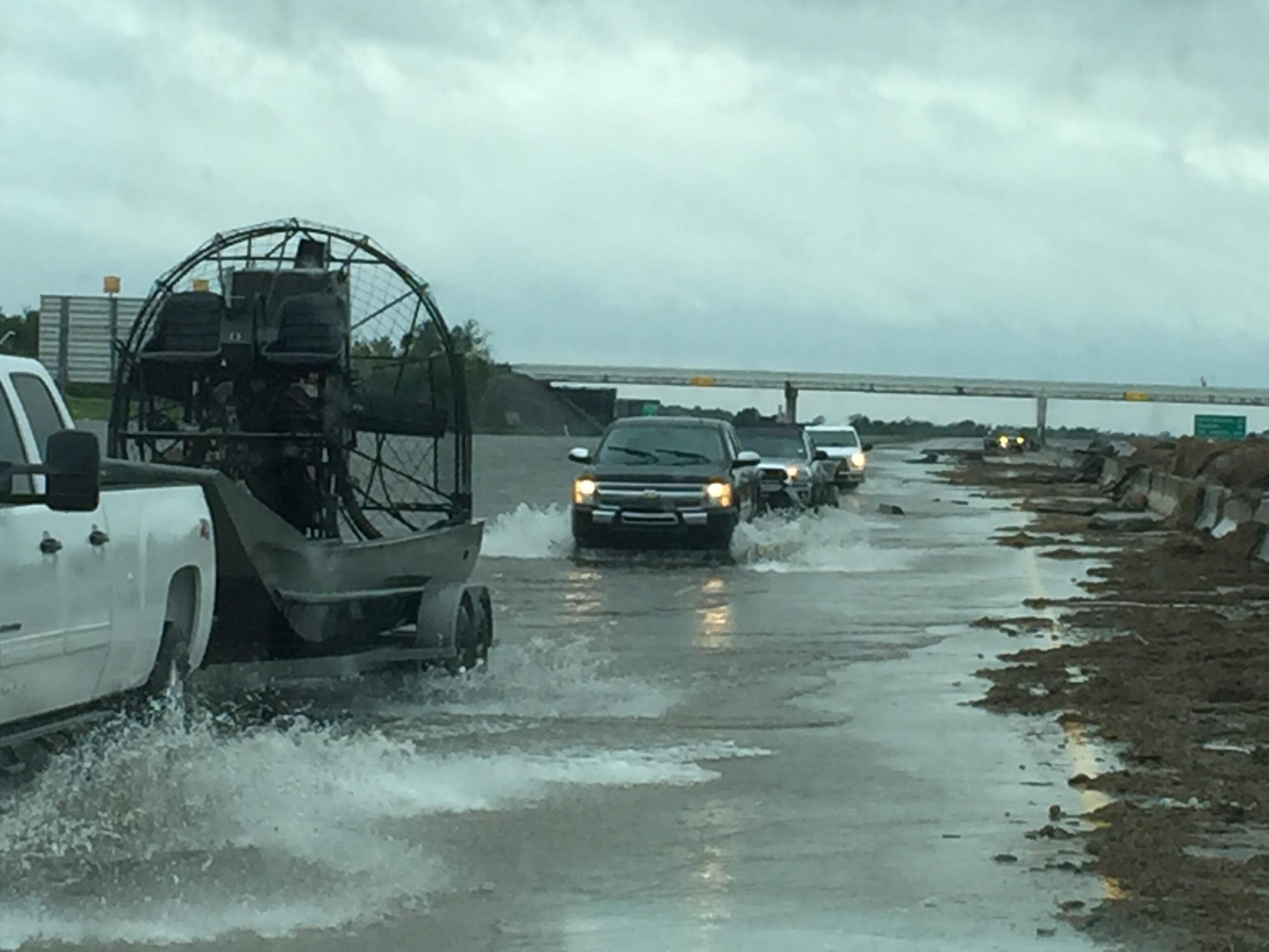 Trucks driving through a flooded highway after storms.